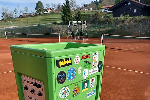Eine grüne Ballwurfmaschine mit Aufklebern steht auf einem Tennisplatz Tennis lernen beim Urlaub im Bayerischen Wald